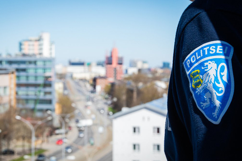 A police officer stands overlooking a cityscape, wearing a uniform featuring a crest. The backdrop shows buildings and roads, symbolizing urban policing and community safety.