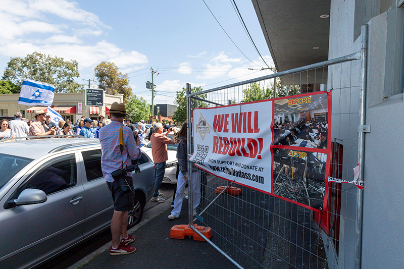 Picture of crowds and fence outside the Adass Synagogue in Melbourne, Australia, with sign saying 'We will rebuild', after recent arson attack