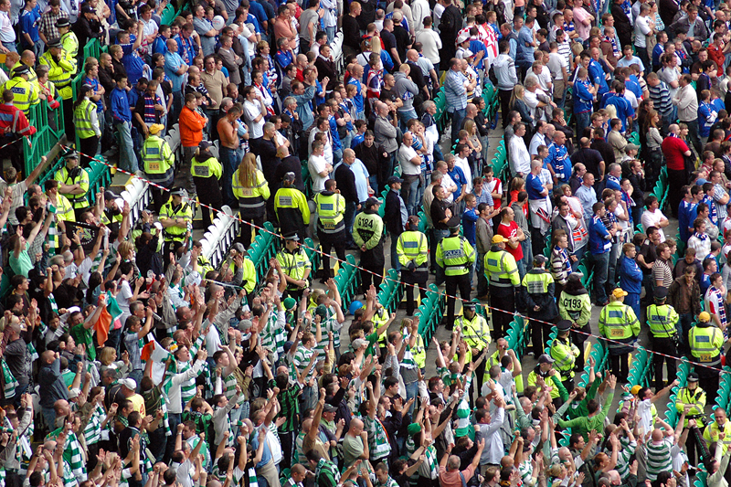 Celtic fans celebrate victory over Rangers fans, while police segregate the two sets of supporters