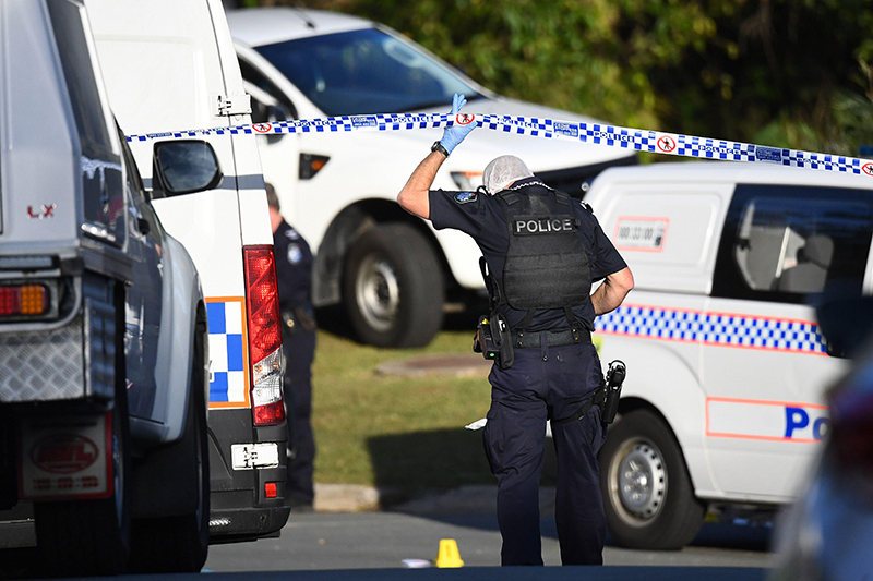 A Queensland Police officer secures a crime scene with tape, surrounded by police vehicles. Evidence markers indicate an investigation is underway, emphasizing the role of law enforcement in ensuring public safety.