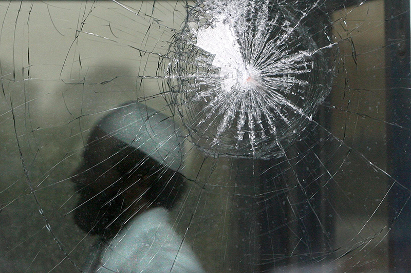 Shattered glass in the window to a mosque, man (blurred) standing behind wearing muslim prayer cap