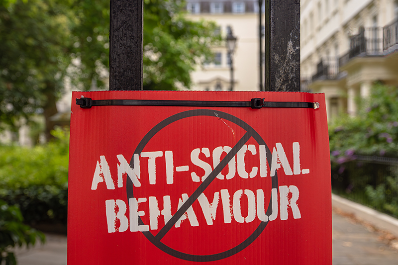 Red sign ANTI-SOCIAL BEHAVIOUR crossed out, urban setting.