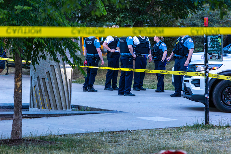 caution tape wrapped around tree blocking access to a crime scene that happen in Chicago during sunset. Police have arrived and are investigation in the background