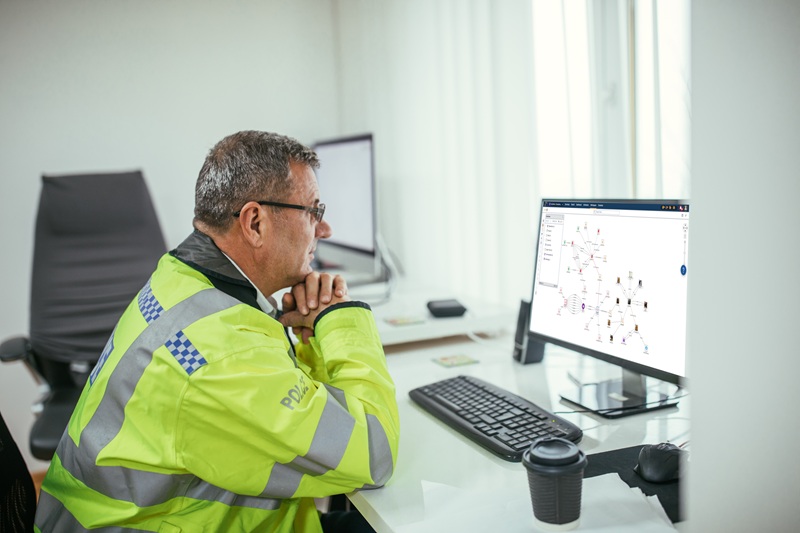 A police officer, wearing a bright jacket, analyzes data on a computer screen. The workspace is modern and focused on using technology for effective policing and insights.