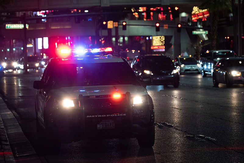 A US patrol car parked at the side of a busy urban road at night, with lights on