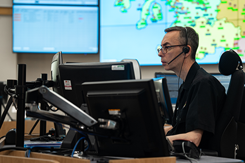 Motorola feature image. A focused operator sits at a desk with multiple monitors, managing data and communications in a busy command center, essential for coordinating police operations and public safety responses.