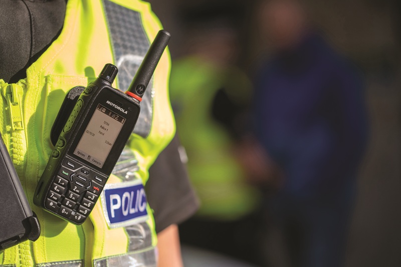 The image shows a police officer wearing a reflective vest, equipped with a Motorola radio. Communication devices are essential for coordinating responses and enhancing public safety.