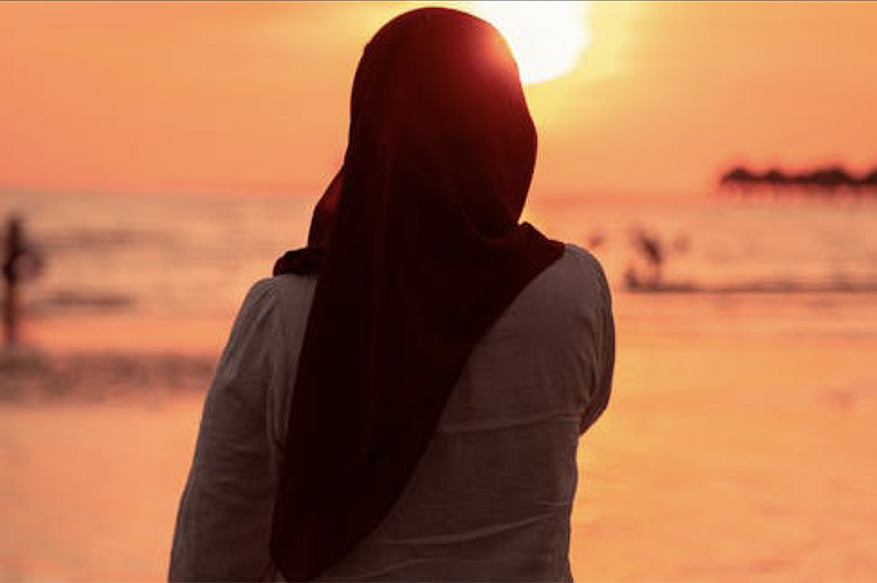 Muslim woman in headscarf pictured from rear, looking into the sun