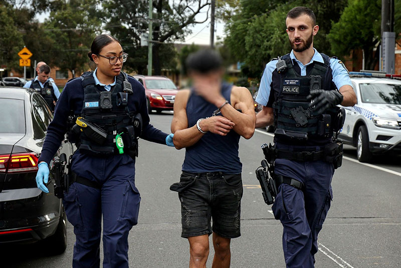 Two NSW Police officers leading away a domestic violence suspect (faced blurred)