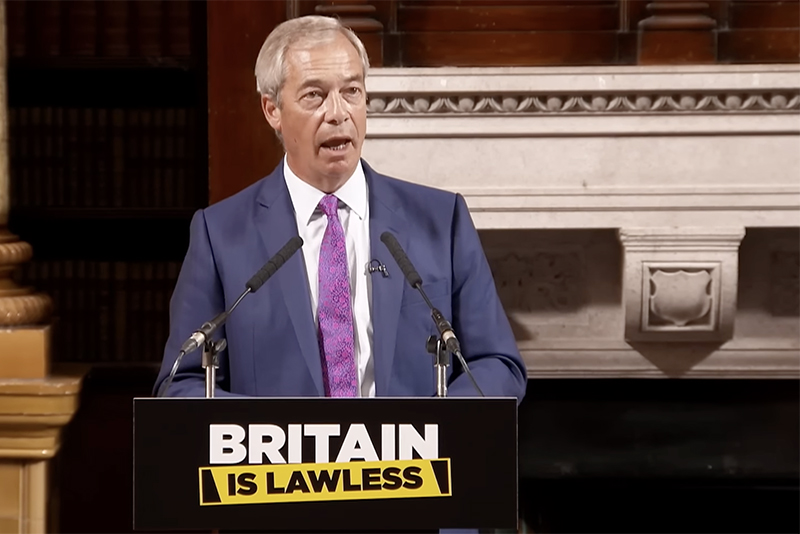 Nigel Farage speaking at a podium that bears the sign 'Britain is lawless'