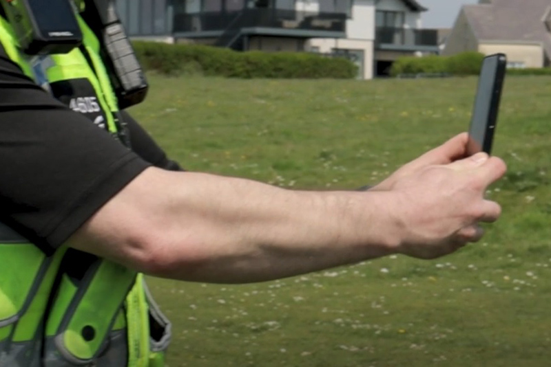 South Wales Police officer holding mobile phone, using operator-initiated facial recognition