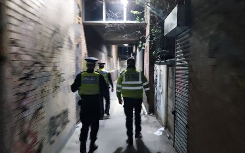 Officers on patrol, viewed from behind, in a lit alleyway in South Yorkshire, as part of a hotspot policing initiative