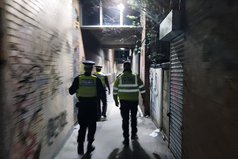 Officers on patrol, viewed from behind, in a lit alleyway in South Yorkshire, as part of a hotspot policing initiative