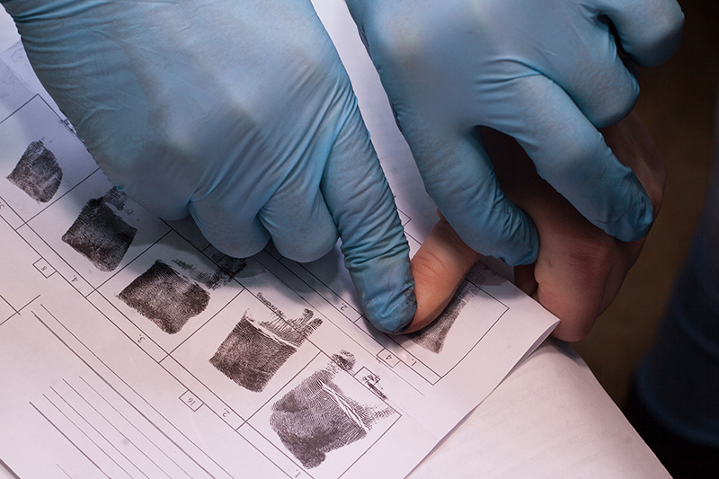 A gloved hand presses a finger onto a fingerprint card, marked with inked prints. This process is crucial for identification in law enforcement records.