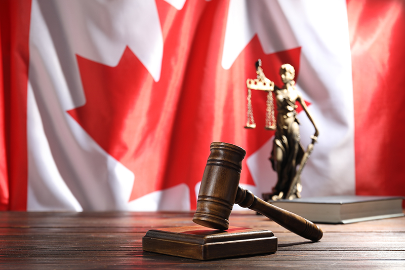 Judge's gavel, book and statue of Lady Justice on wooden table against flag of Canada, closeup