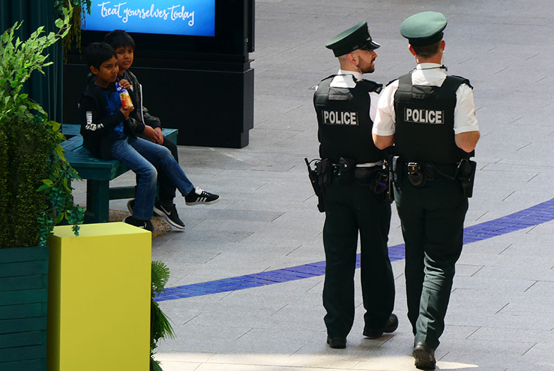 Two Police Service of Northern Ireland officers patrolling in the Victoria Square Centre in Belfast, watched by two children