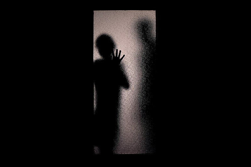 Man and woman or child in silhouette, behind frosted glass door, suggesting family conflict or child sexual exploitation