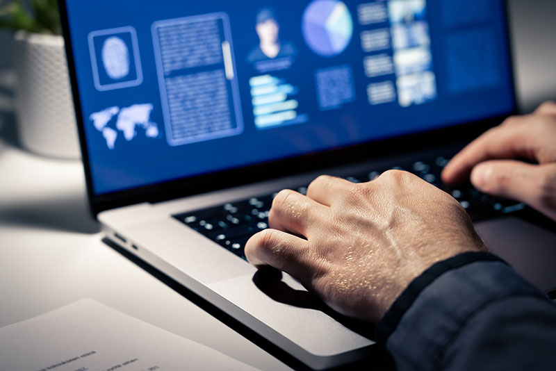 Pair of hands on laptop keyboard typing in data to an offender profile, signifying criminal case investigation