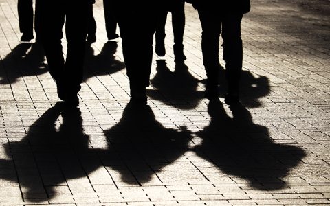 Silhouettes and shadows of people on the city street. Crowd walking down on sidewalk, concept of strangers, crime, society, gang or population