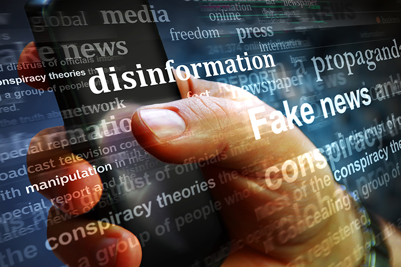 A hand holds a smartphone amidst floating words like "disinformation," "fake news," and "propaganda," highlighting concerns about misinformation in media and its impact on public perception and policing.