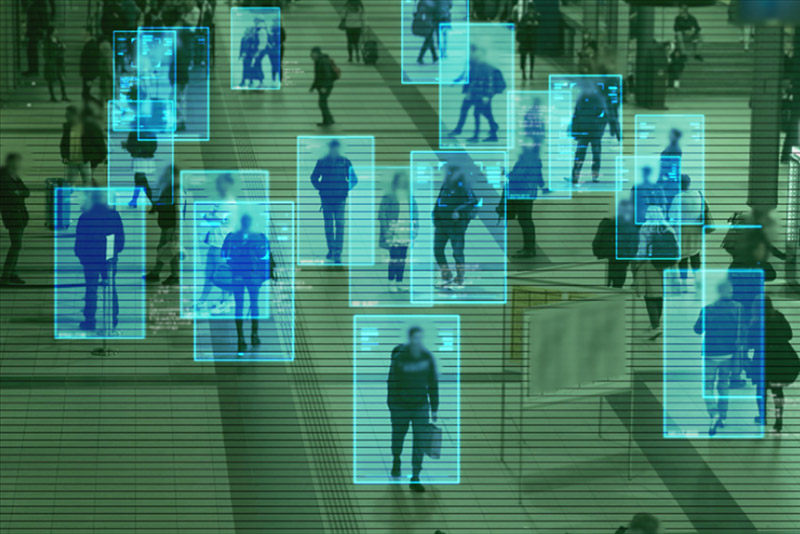 The image shows a crowded space, overlaid with digital outlines of people, symbolizing advanced surveillance technology’s role in policing and public safety.