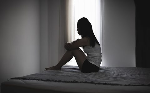 Female in silhouette sitting alone of a bed, concept to domestic abuse and coercive control