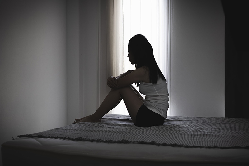 Female in silhouette sitting alone of a bed, concept to domestic abuse and coercive control
