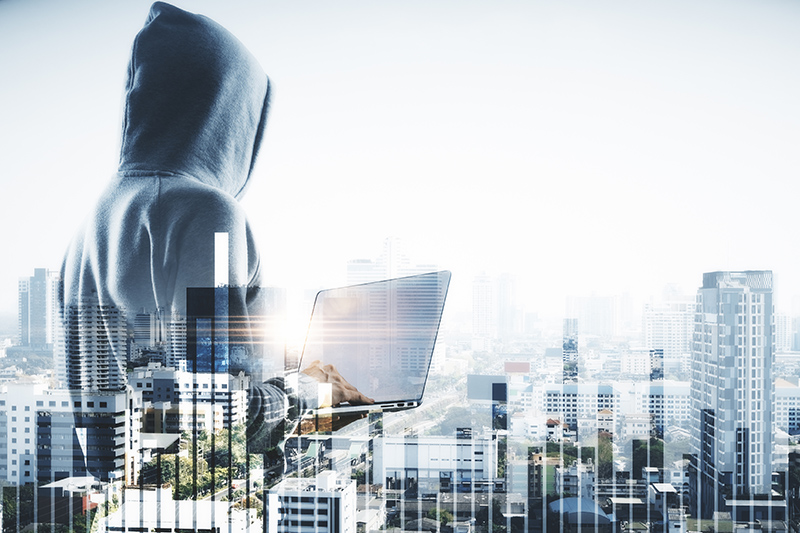 A hooded figure with a laptop overlooks a city, symbolizing the intersection of technology and financial crime, highlighting policing challenges in urban environments as discussed on policinginsight.com.