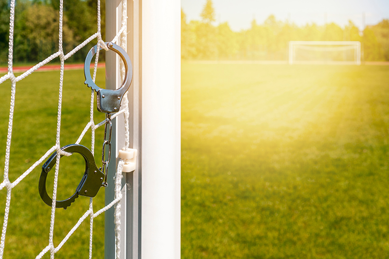 Goal net on a football pitch with a pair of handcuffs hanging from them, symbolising football-related crime