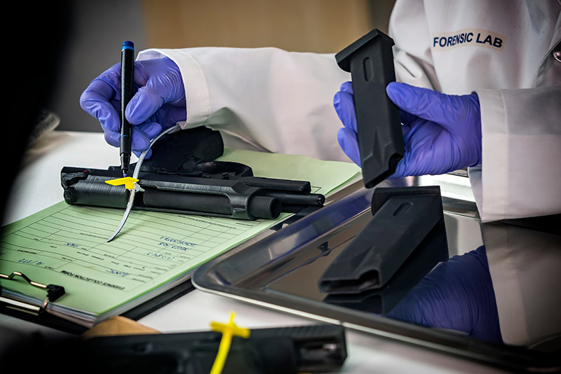 Police scientist notes serial number on sealed firearm in crime lab, conceptual image