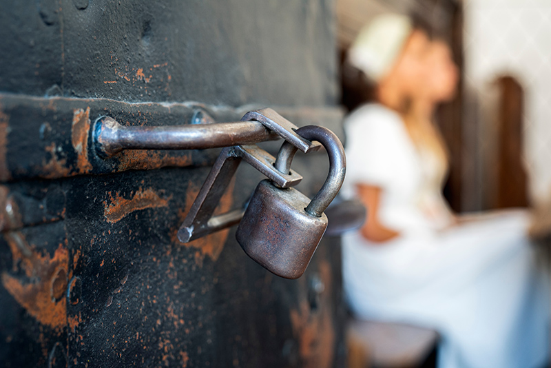 Steel door with padlock, behind it blurred figures of young women, human trafficking and captivity and exploitation concept