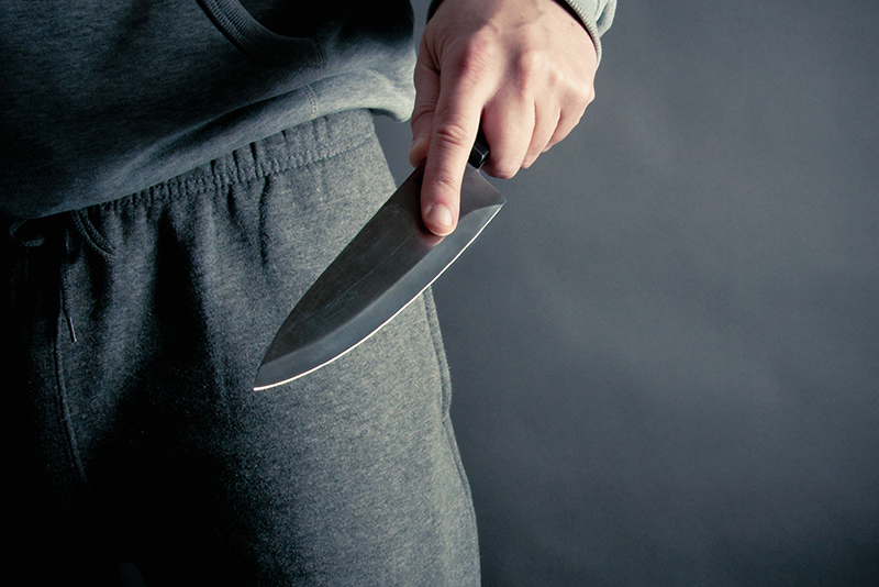 The image depicts a hand gripping a knife near the waist, suggesting a potential threat. In the context of policing, it highlights concerns around weapon possession and public safety.