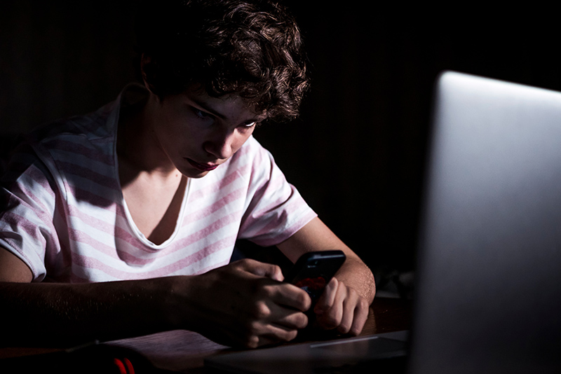 young boy watching phone late in the night in dark bedroom