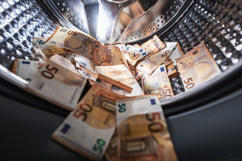 The image depicts various euro banknotes scattered inside a washing machine, symbolizing money laundering and illicit financial activities, relevant themes in law enforcement discussions.