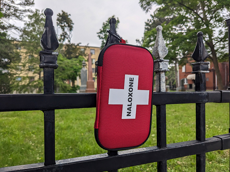 Free kit box of opiate reversal drug naloxone hanging on the fence in city urban area park in Toronto Canada.