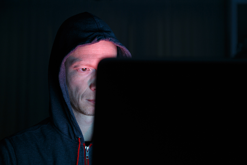 man (face partially obscured) staring at computer screen in darkened room, criminal intent