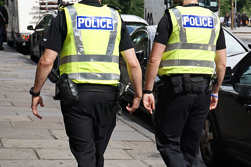 Two police officers in bright yellow and black uniforms walk together on a city street, emphasizing their presence and role in community safety and law enforcement.