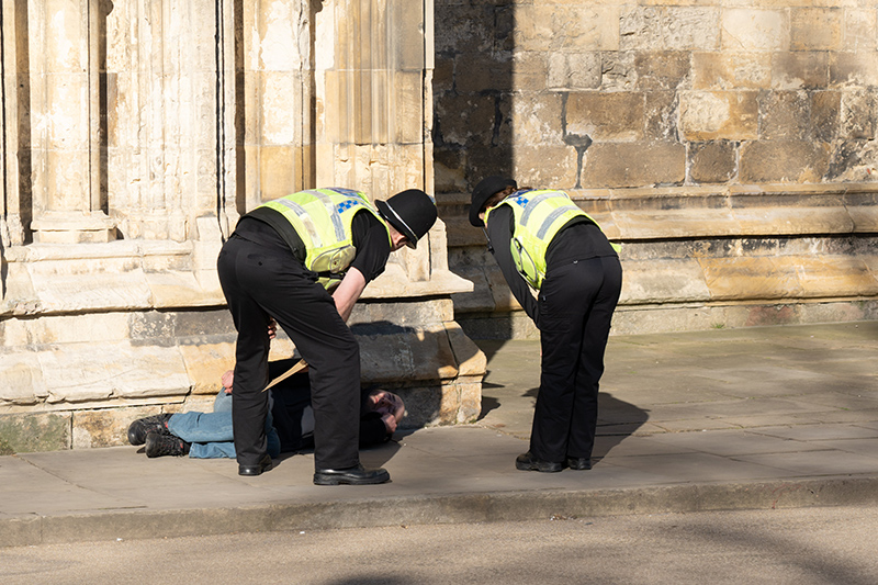 Two uniform police officers checking on the welfare of a man laying on the pavement