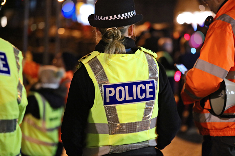 Rear view of a policewoman in hi-visibility jacket policing crowd control at an outside UK event