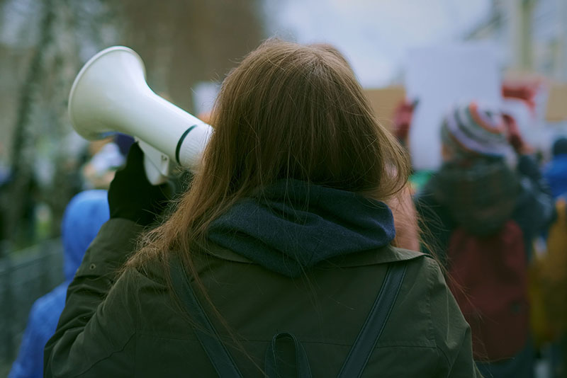 Rear view of young adult female demonstrator shouting into megaphone