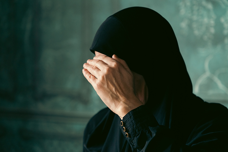 muslim woman wearing hijab covering her face with hand
