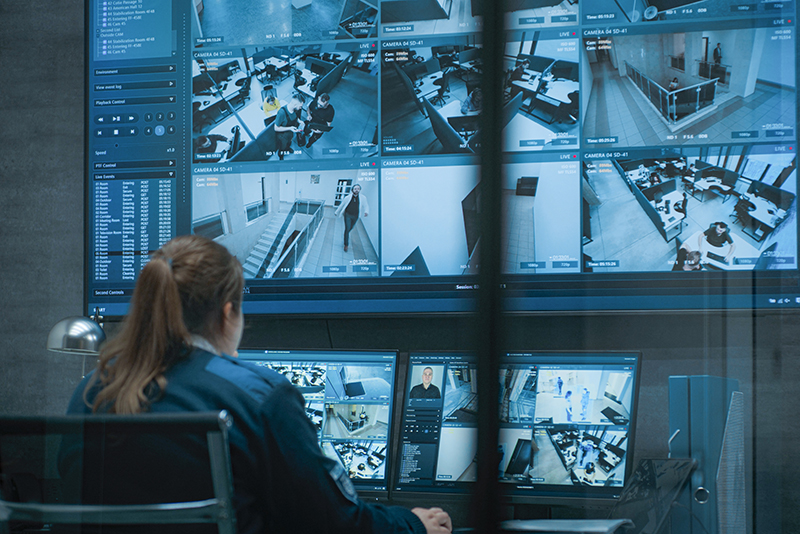 Female CCTV operator works on computer and tablet in monitoring center with security cameras