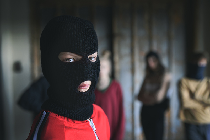 Boy with mask with teenagers gang indoors in abandoned building, looking at camera.