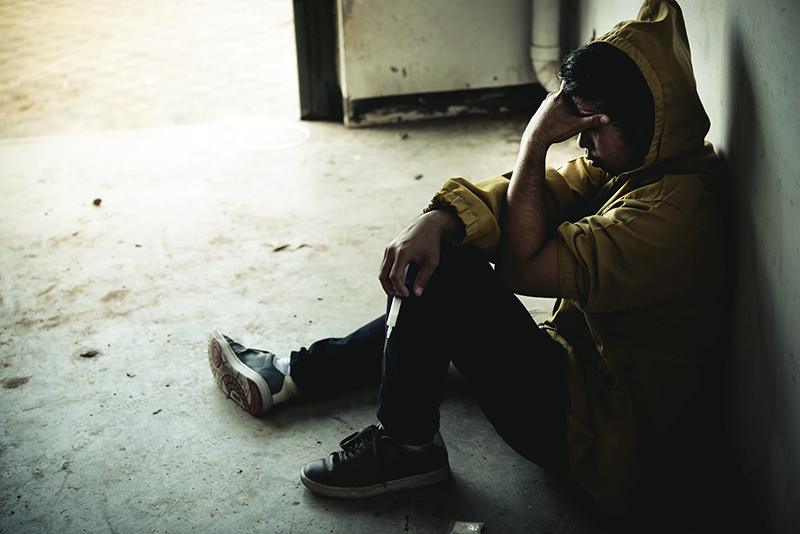 Dishevelled teenager sitting on the floor, back against the wall, with syringe in hand - concept of drug addiction or cuckooing