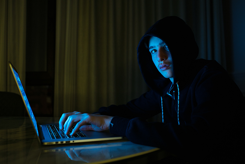 Young boy in a dark room with laptop, online crime, hacking