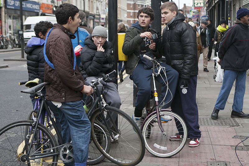 Four teenage boys sitting on bikes on a street corner