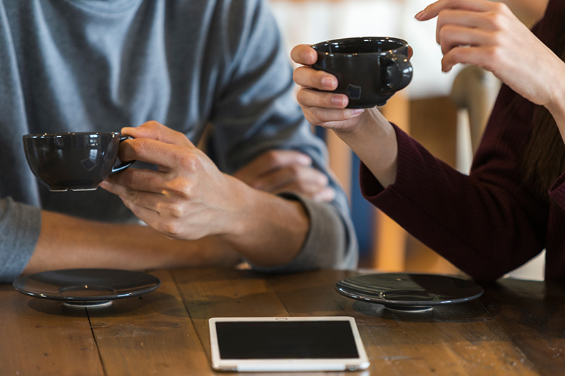 Two people sitting at a table sharing coffee, and chatting, no faces visible