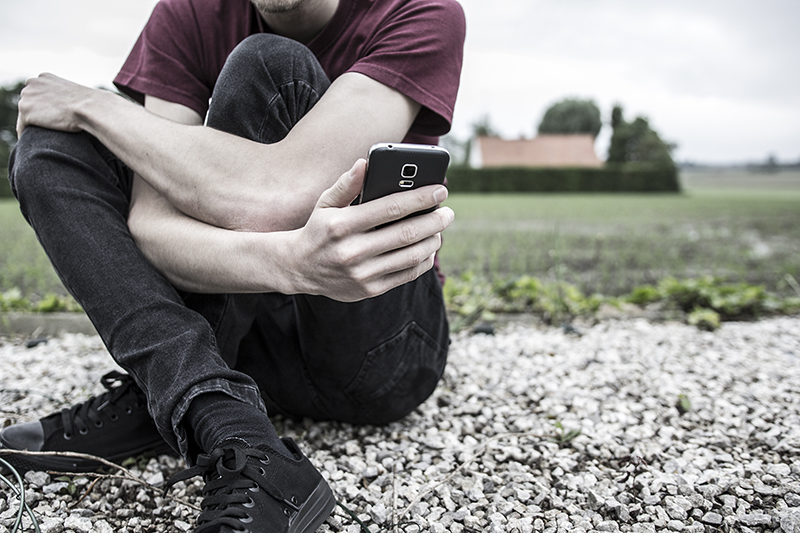 An anonymous young man holding his phone and looking at it, concept of online bullying or county lines drug dealing