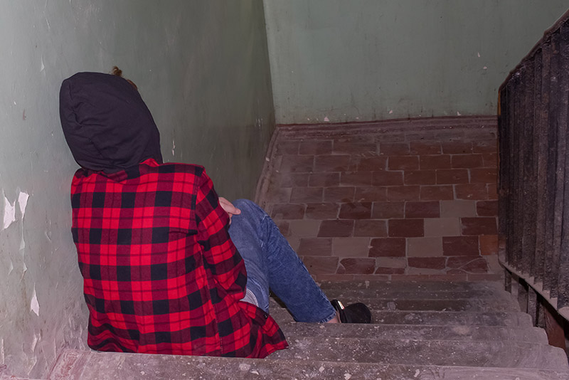 rear view of an upset teenager sitting on the stairs alone.