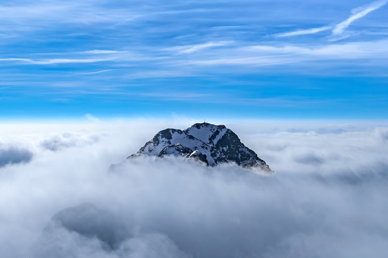 Panoramic view from Monte Zoncolan of a mountain peak, surrounded by clouds like an island